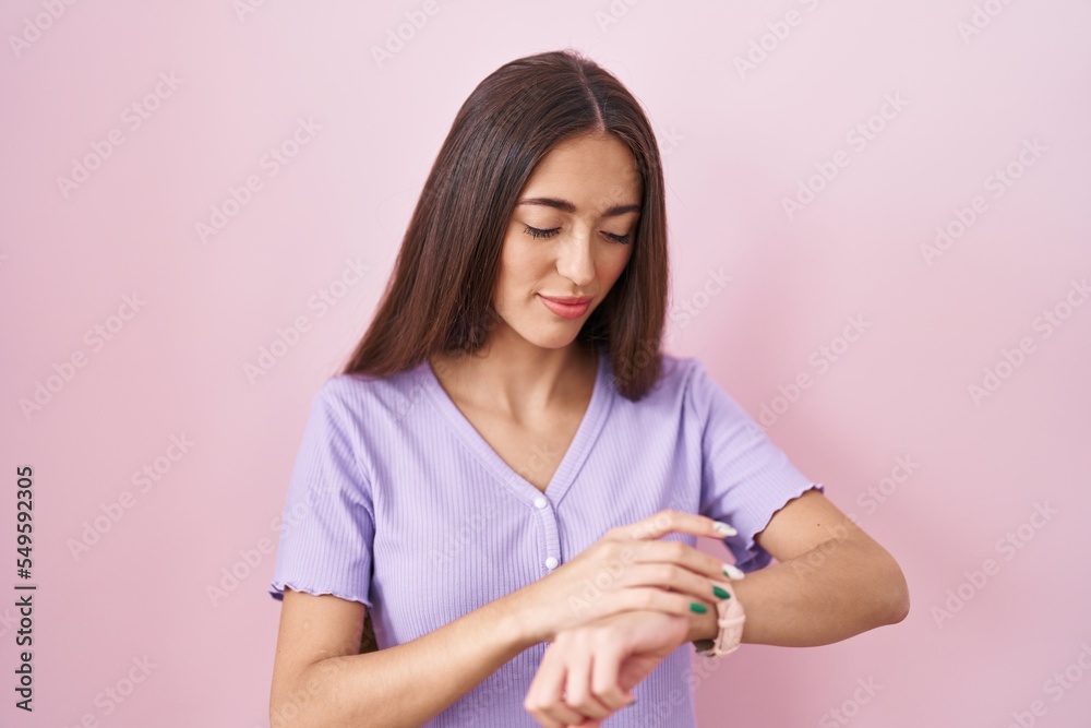 Young hispanic woman with long hair standing over pink background checking the time on wrist watch, relaxed and confident Young hispanic woman with long hair standing over pink background checking the time on wrist watch, relaxed and confident