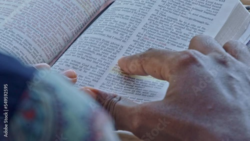 A lady's fingers points to Bible verses while she reads the page.