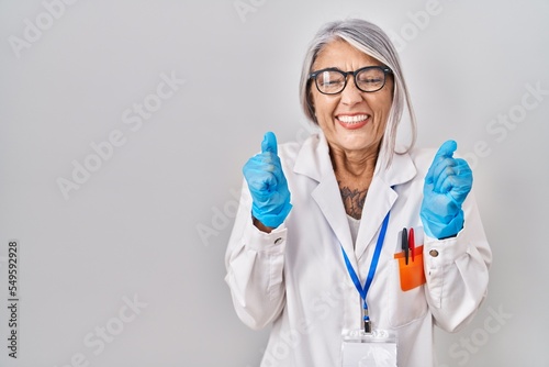 Middle age woman with grey hair wearing scientist robe excited for success with arms raised and eyes closed celebrating victory smiling. winner concept.