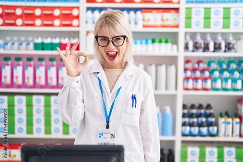 Young caucasian woman working at pharmacy drugstore smiling positive doing ok sign with hand and fingers. successful expression.