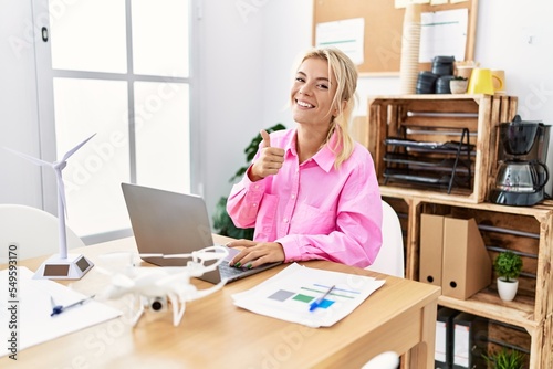 Young caucasian woman working at the office doing happy thumbs up gesture with hand. approving expression looking at the camera showing success.