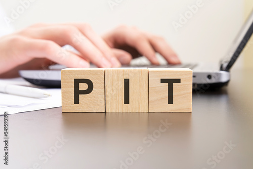 pit - acronym from wooden blocks with letters. background hands on a laptop with blur. business concept. photo
