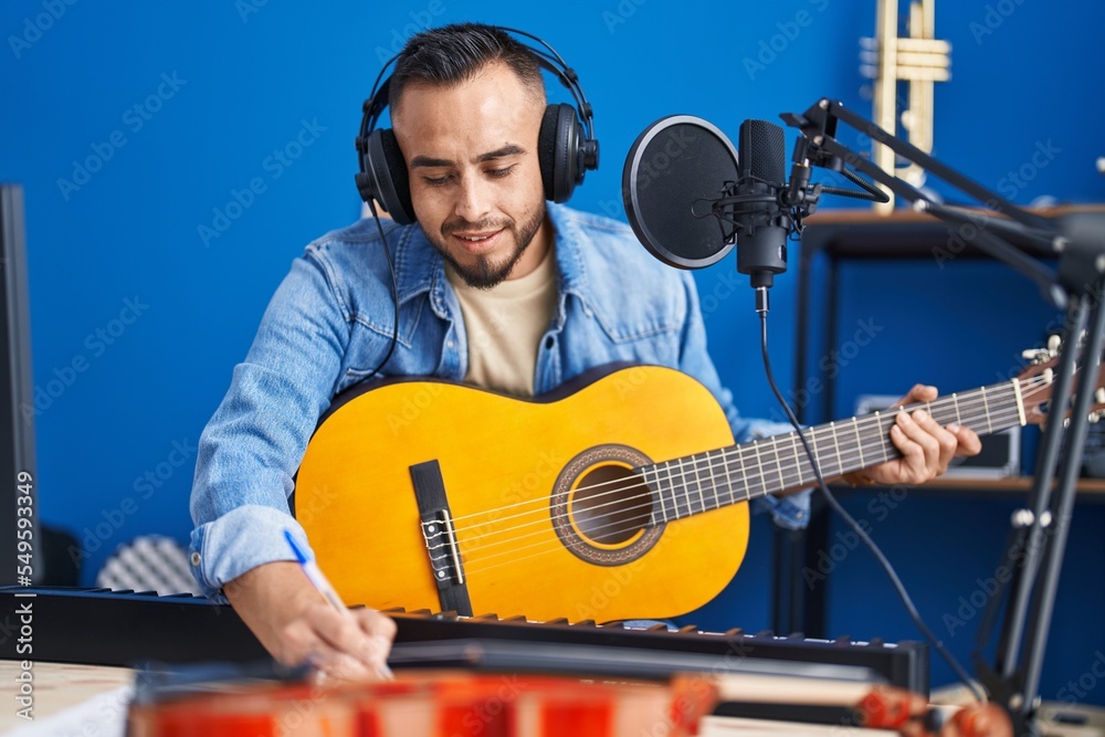Fototapeta premium Young hispanic man artist composing song playing classical guitar at music studio