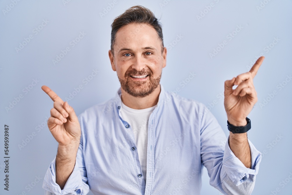 Middle age caucasian man standing over blue background smiling confident pointing with fingers to different directions. copy space for advertisement Middle age caucasian man standing over blue background smiling confident pointing with fingers to different directions. copy space for advertisement