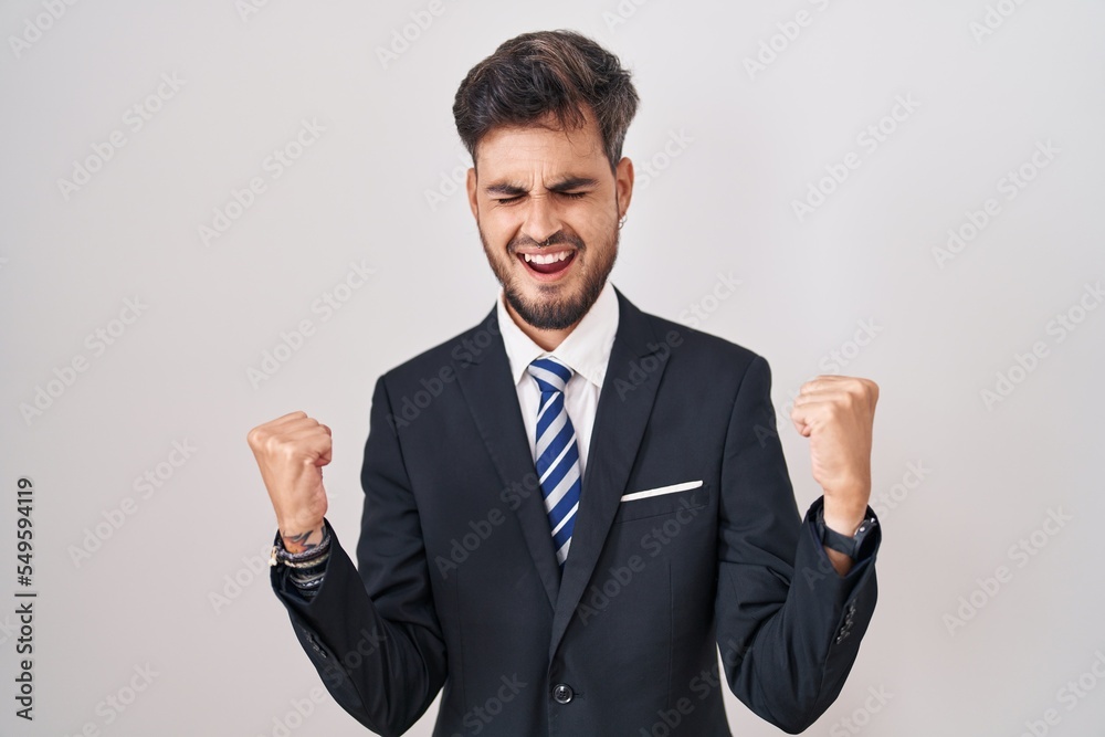 Young hispanic man with tattoos wearing business suit and tie celebrating surprised and amazed for success with arms raised and eyes closed. winner concept. Young hispanic man with tattoos wearing business suit and tie celebrating surprised and amazed for success with arms raised and eyes closed. winner concept.