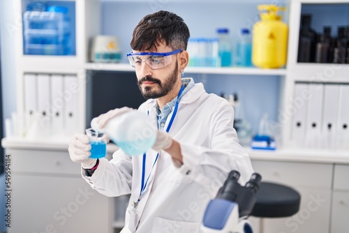 Young hispanic man scientist pouring liquid on glass at laboratory