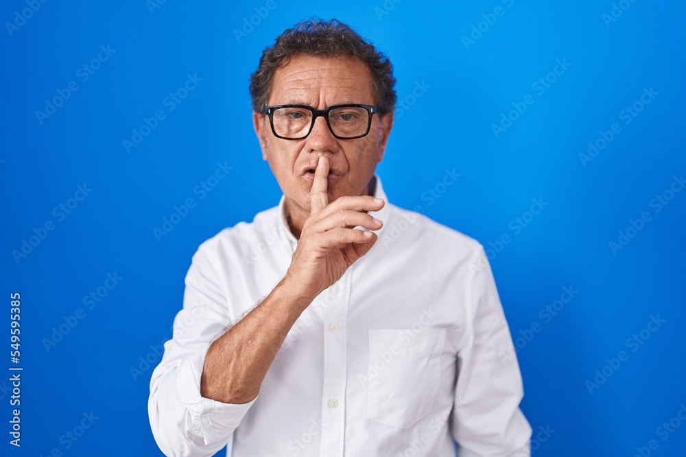 Middle age hispanic man standing over blue background asking to be quiet with finger on lips. silence and secret concept. Middle age hispanic man standing over blue background asking to be quiet with finger on lips. silence and secret concept.
