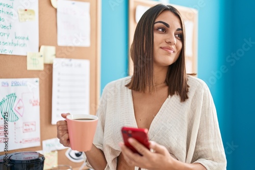 Young beautiful hispanic woman business worker using smartphone drinking coffee at office