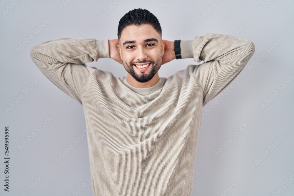 Young handsome man standing over isolated background relaxing and stretching, arms and hands behind head and neck smiling happy Young handsome man standing over isolated background relaxing and stretching, arms and hands behind head and neck smiling happy