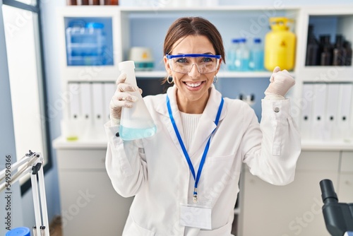 Young brunette woman working at scientist laboratory screaming proud  celebrating victory and success very excited with raised arm