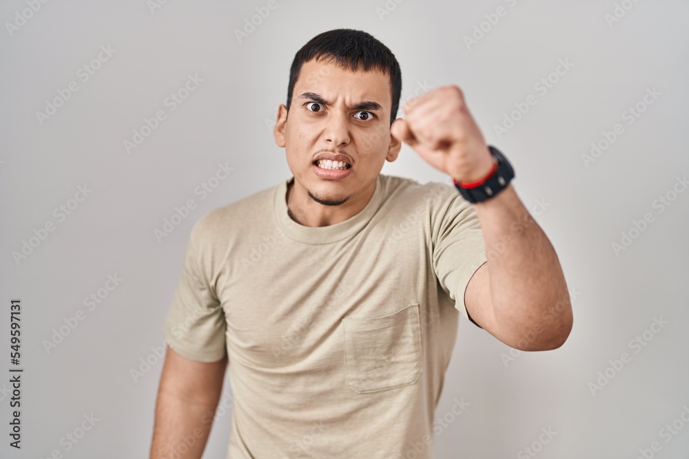 Young arab man wearing casual t shirt angry and mad raising fist frustrated and furious while shouting with anger. rage and aggressive concept. Young arab man wearing casual t shirt angry and mad raising fist frustrated and furious while shouting with anger. rage and aggressive concept.