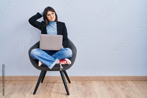 Fotografie Young hispanic woman sitting on chair using computer laptop confuse and wondering about question