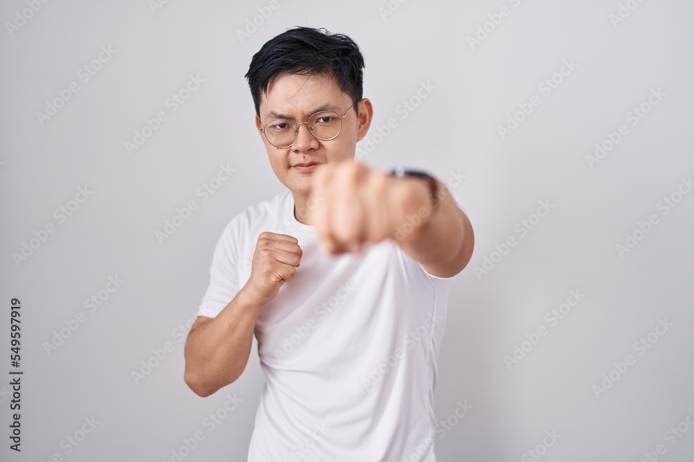 Young asian man standing over white background punching fist to fight, aggressive and angry attack, threat and violence Young asian man standing over white background punching fist to fight, aggressive and angry attack, threat and violence