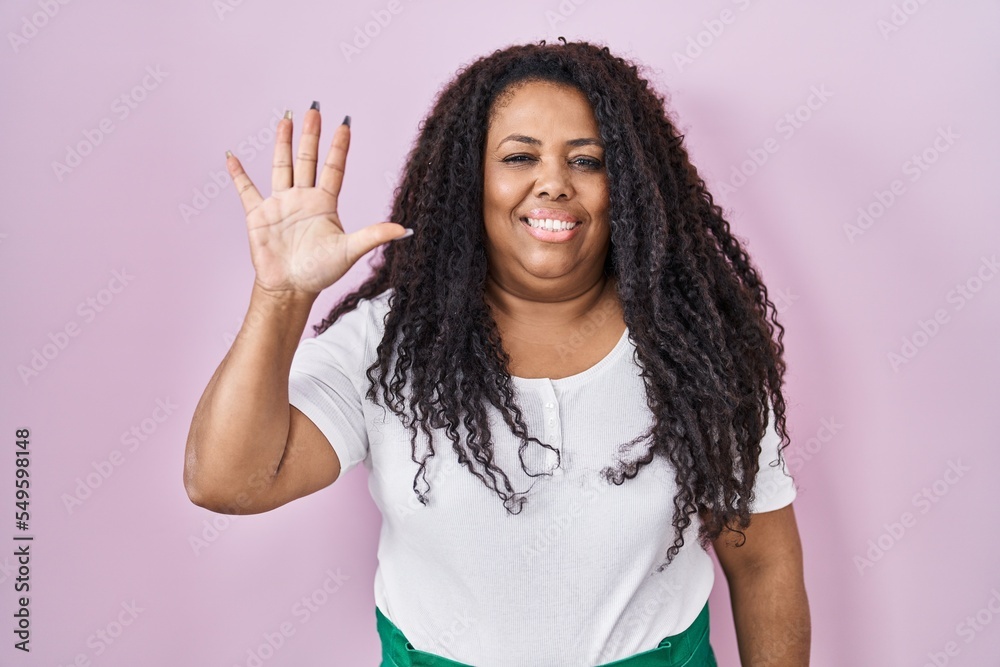 Plus size hispanic woman standing over pink background showing and pointing up with fingers number five while smiling confident and happy. Plus size hispanic woman standing over pink background showing and pointing up with fingers number five while smiling confident and happy.