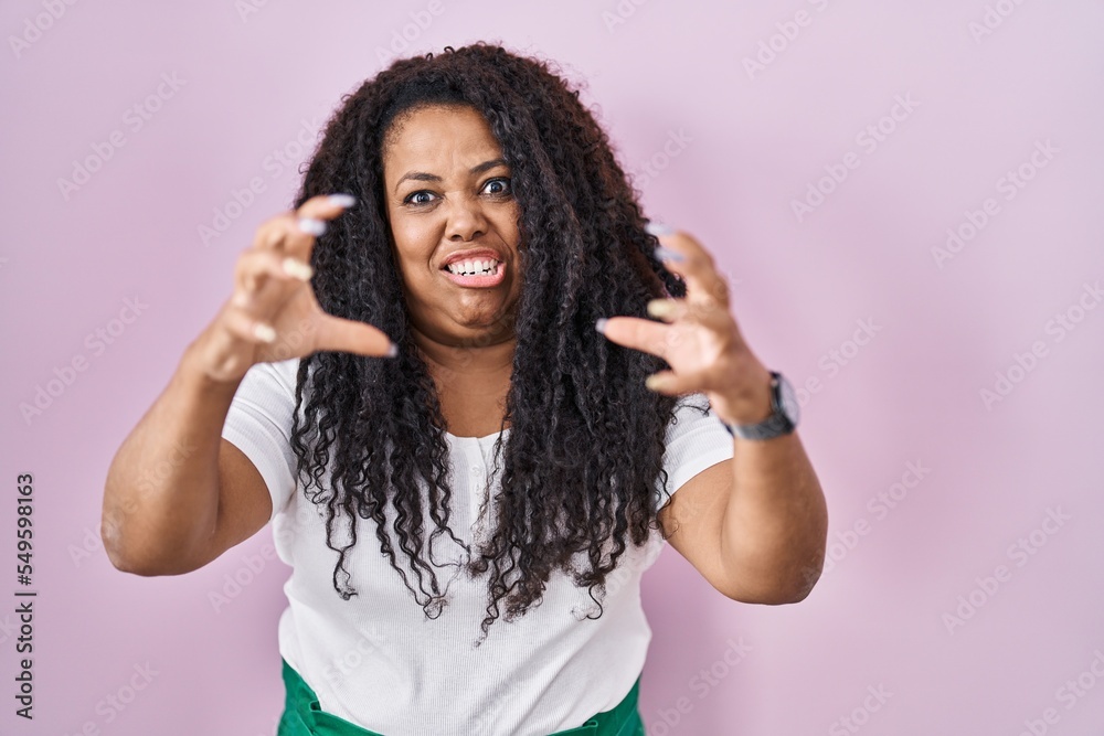 Plus size hispanic woman standing over pink background shouting frustrated with rage, hands trying to strangle, yelling mad Plus size hispanic woman standing over pink background shouting frustrated with rage, hands trying to strangle, yelling mad