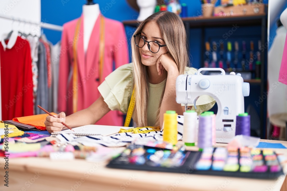 Fototapeta premium Young beautiful hispanic woman tailor smiling confident drawing on notebook at clothing factory