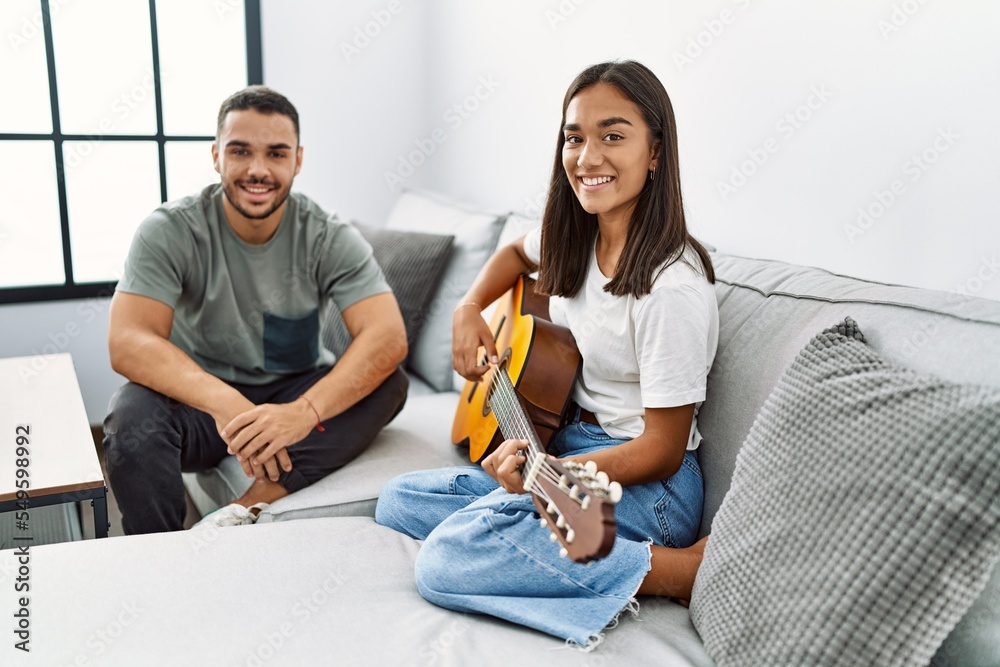 Young latin couple playing classical guitar sitting on the sofa at home. Young latin couple playing classical guitar sitting on the sofa at home.