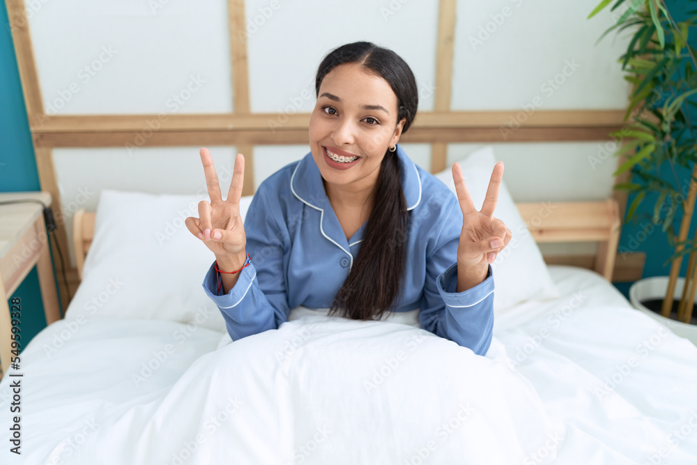 Young arab woman doing victory gesture sitting on bed at bedroom Young arab woman doing victory gesture sitting on bed at bedroom
