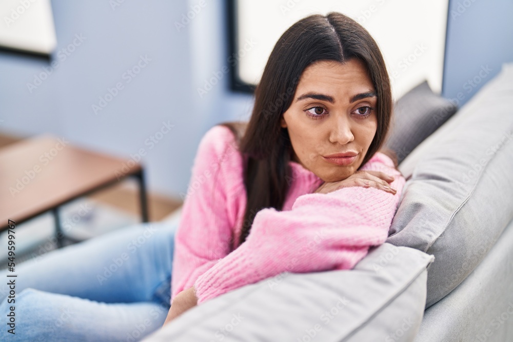 Young hispanic woman with boring expression sitting on sofa at home Young hispanic woman with boring expression sitting on sofa at home