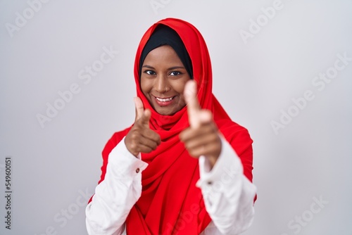 Young arab woman wearing traditional islamic hijab scarf pointing fingers to camera with happy and funny face. good energy and vibes.