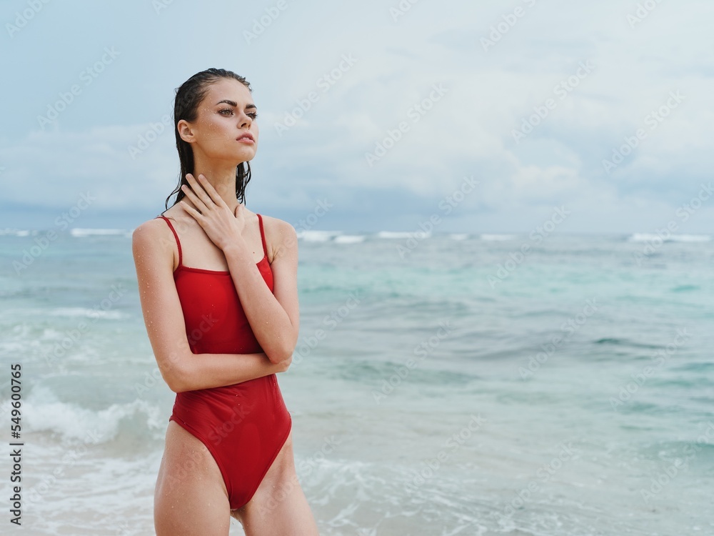 Beautiful sexy woman in a red swimsuit on the ocean beach with wet hair, slender pumped body sunscreen Beautiful sexy woman in a red swimsuit on the ocean beach with wet hair, slender pumped body sunscreen
