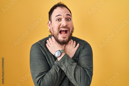 Plus size hispanic man with beard standing over yellow background shouting suffocate because painful strangle. health problem. asphyxiate and suicide concept.
