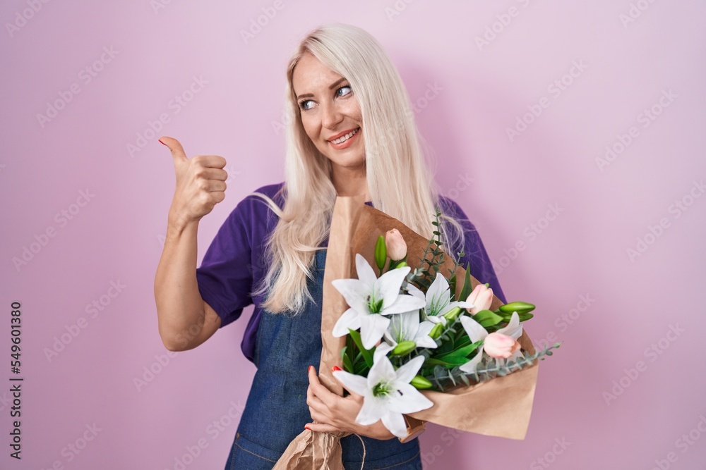 Caucasian woman holding bouquet of white flowers smiling with happy face looking and pointing to the side with thumb up. Caucasian woman holding bouquet of white flowers smiling with happy face looking and pointing to the side with thumb up.