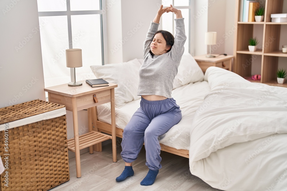 Young woman with down syndrome waking up stretching arms at bedroom