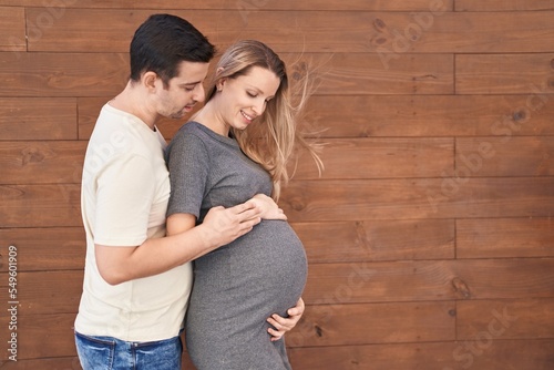 Man and woman couple hugging each other expecting baby over isolated wooden background