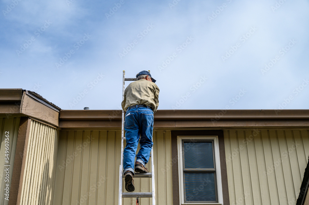Senior man climbing an aluminum extension ladder to a home rooftop
