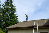 Fall maintenance, senior man on a residential house roof with a gas powered leaf blower cleaning off leaves and pine needles
