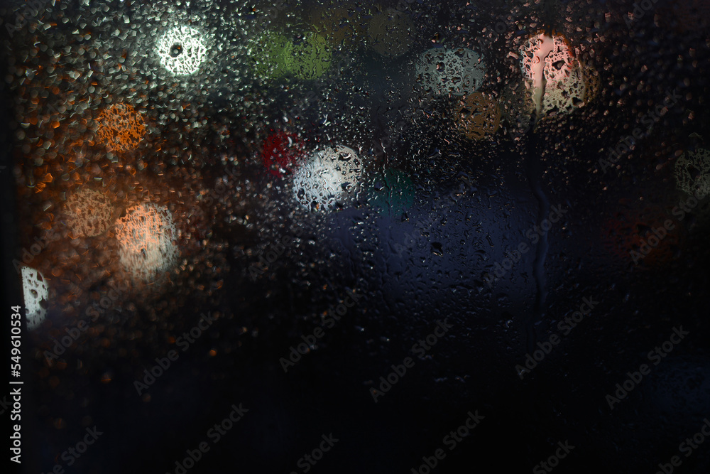 Obraz premium Raindrops on a window glass and unfocused lights of night city. Dark Blurred Background of night city behind glass during rain
