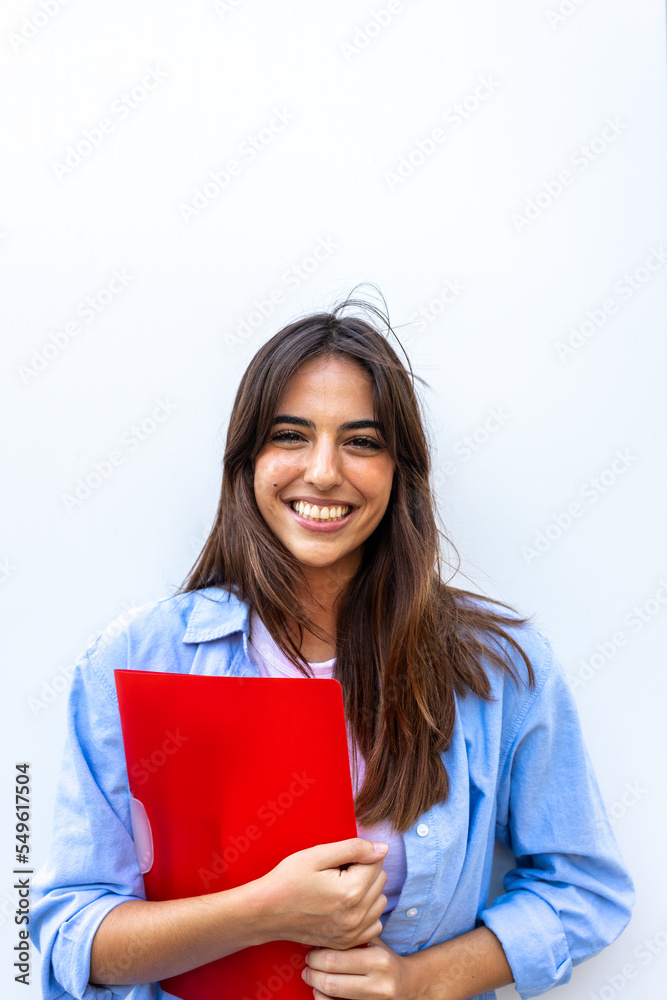 Vertical portrait of happy, smiling female university student looking at camera holding red folder. Vertical portrait of happy, smiling female university student looking at camera holding red folder.