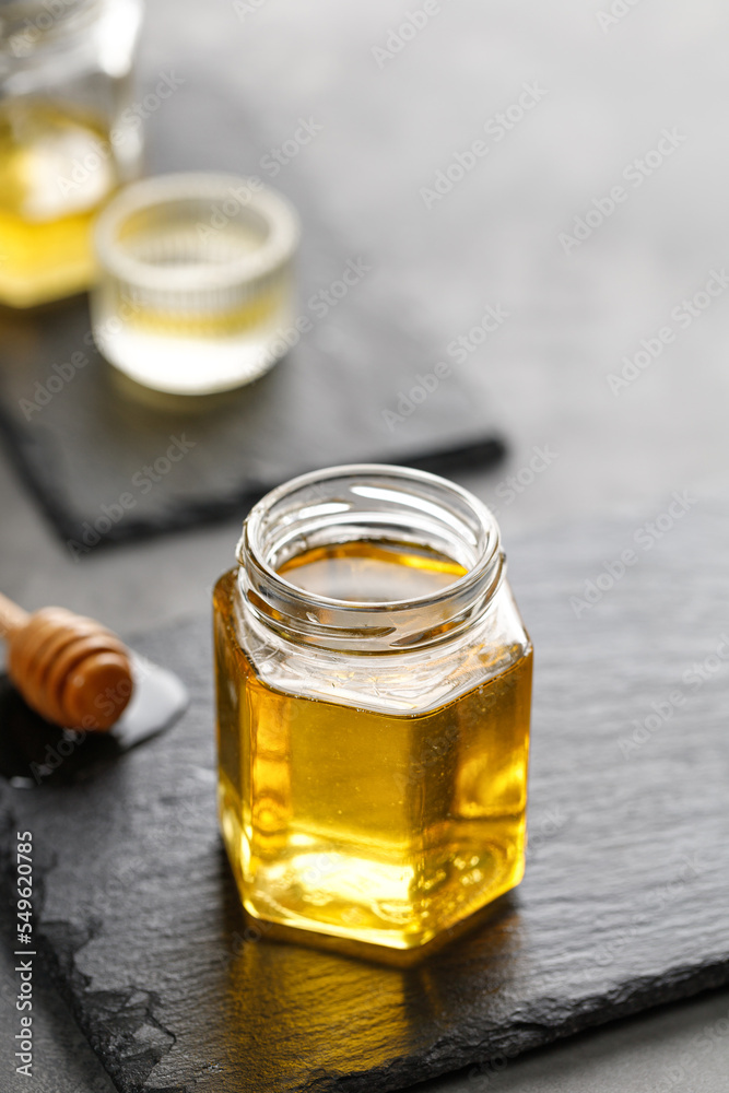 Glass jar of honey with wooden honey dipper, drizzler on a dark slate board and black background. Superfood, Alternative of sugar. Copy space, text. Glass jar of honey with wooden honey dipper, drizzler on a dark slate board and black background. Superfood, Alternative of sugar. Copy space, text.