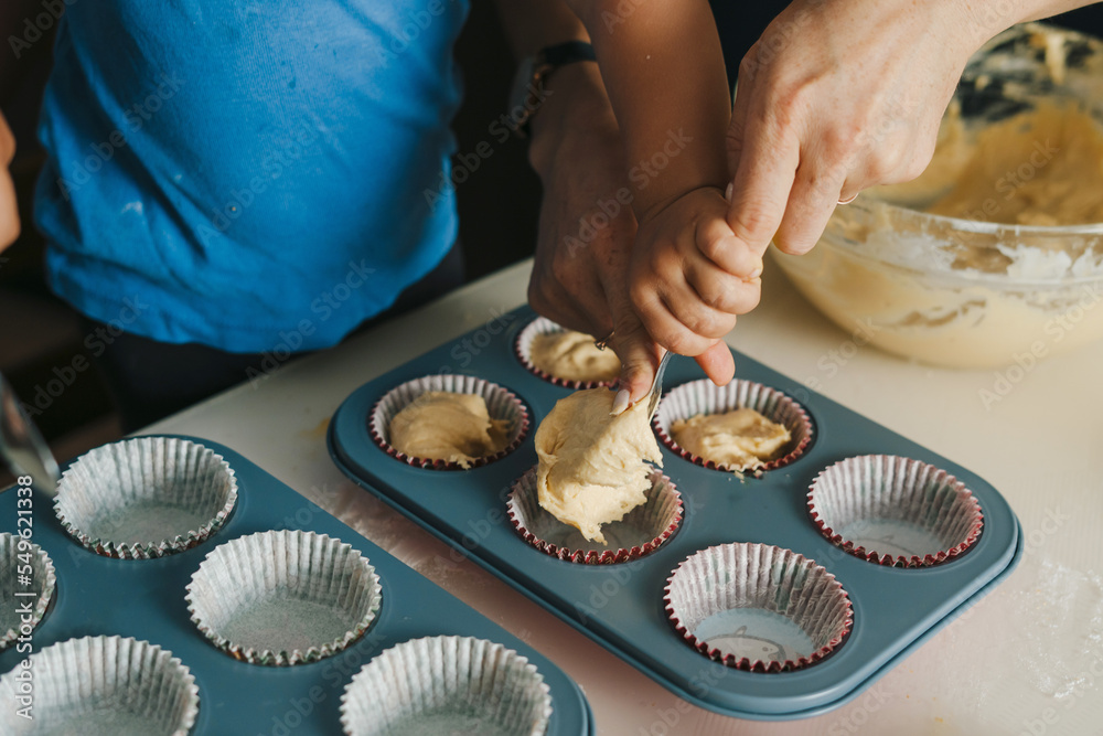 The hands of a mother and a baby child learning how to fill muffin tins