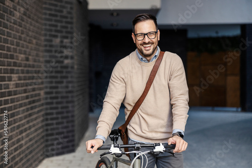 A happy urban businessman is standing on the street with his bicycle.