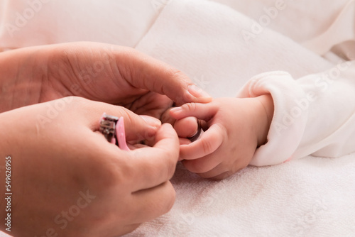 Closeup mother hand holding nail clipper cutting newborn baby nails on tiny fingers while adorable infant sleeping  keep clean with love and care  Parenthood and Motherhood. Healthy Happy Family.