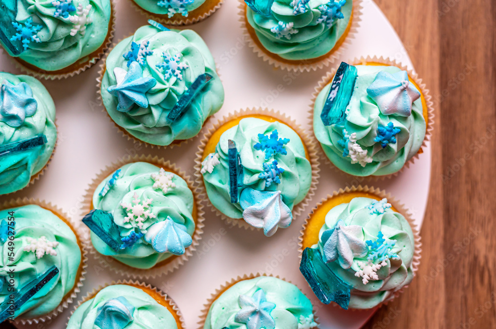 Homemade cupcake of blue color placed on wooden desk. Winter and christmas theme, snowflakes on cream with blue ice. Fresh and home baked sweet. Homemade cupcake of blue color placed on wooden desk. Winter and christmas theme, snowflakes on cream with blue ice. Fresh and home baked sweet.