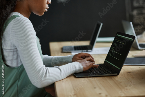Close-up of african American schoolgirl sitting at table and typing codes on laptop at class