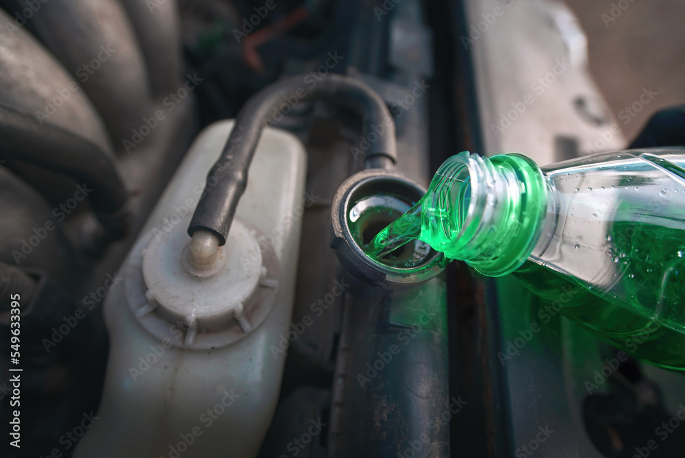 Green coolant pour from plastic bottle into car radiator. Hand filling
