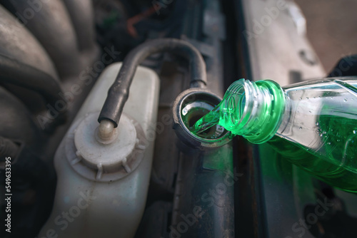 Green coolant pour from plastic bottle into car radiator. Hand filling car cooling system with coolant for cold season. Filling vehicle with new antifreeze. Vehicle coolant level, car radiator system