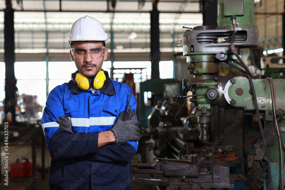 Technician engineer man in protective suit standing and arm crossed while looking camera and controlling or maintenance operation work lathe metal machine at heavy industry manufacturing factory Technician engineer man in protective suit standing and arm crossed while looking camera and controlling or maintenance operation work lathe metal machine at heavy industry manufacturing factory