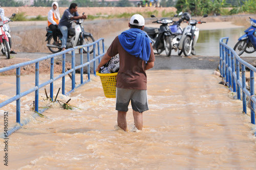 Obraz na plátně a man wading through the flood carrying a basket of clothes