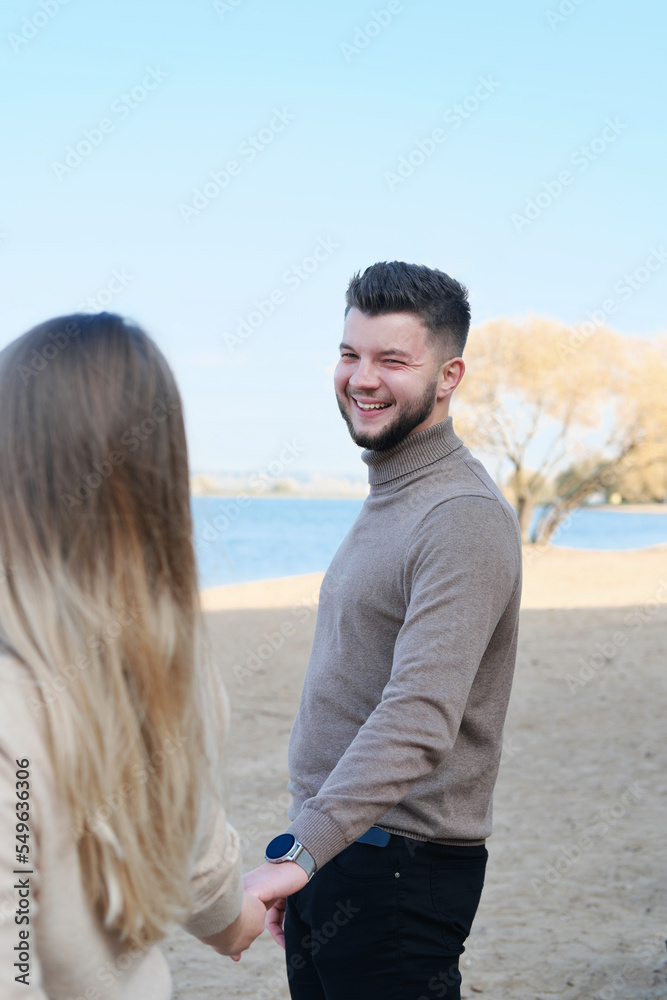 Young man and woman holding hands and posing on the beach. The guy looks at the girl and smiles
