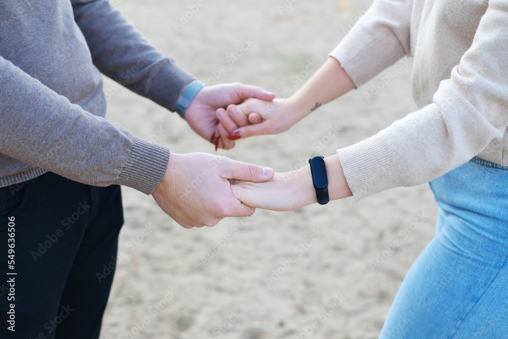 Young man and woman hold hands on the background of the beach sand. Close-up of hands