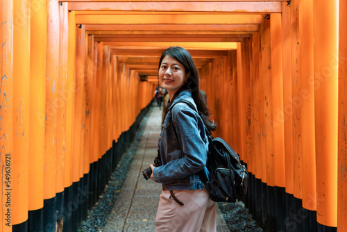 pretty asian Japanese woman backpacker turning to smile at camera while taking the fushimi inari hike with red torii gates in Kyoto japan