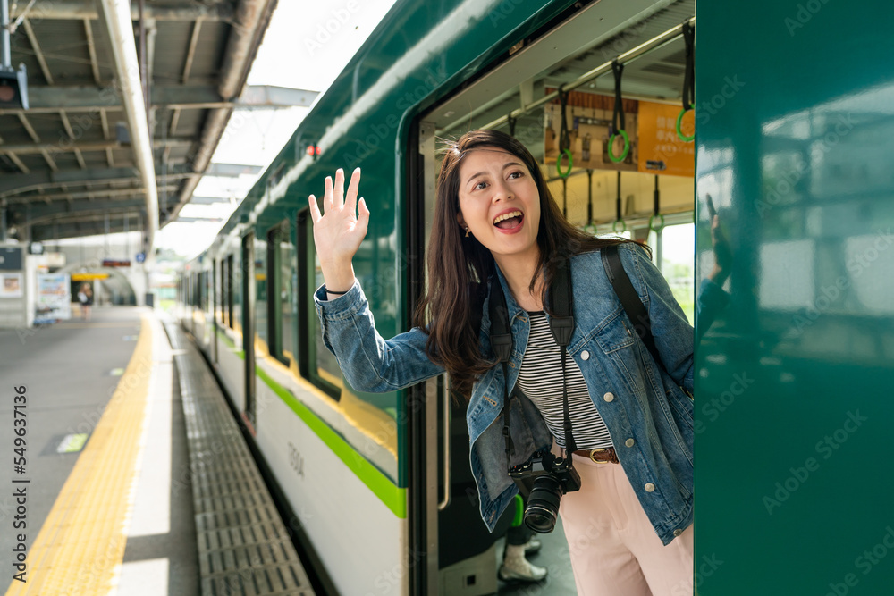 happy asian Japanese female passenger standing in the train car and looking out to wave hand at friend in distance, ready to leave at uji station in Kyoto japan