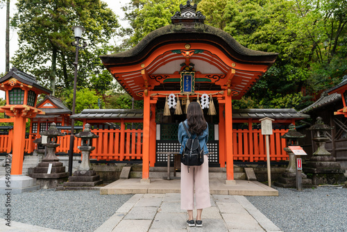 rear view with full length of devout asian Japanese woman standing and praying in front of red Shinto shrine at Fushimi Inari Taisha shrine in Kyoto japan at springtime