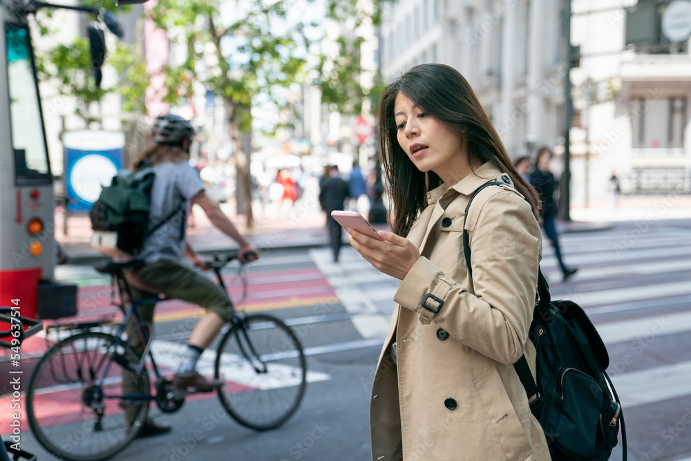 asian chinese business woman stopping to check message on the phone as she is heading to work on the street in san Francisco California usa with a male cyclist at background