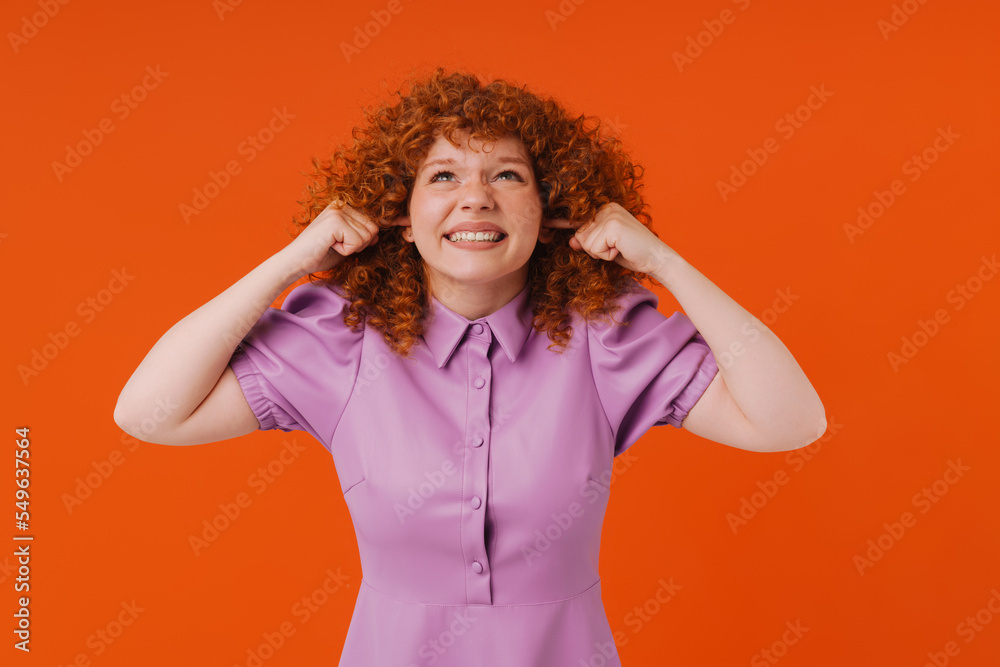 White ginger woman grimacing while plugging her ears White ginger woman grimacing while plugging her ears